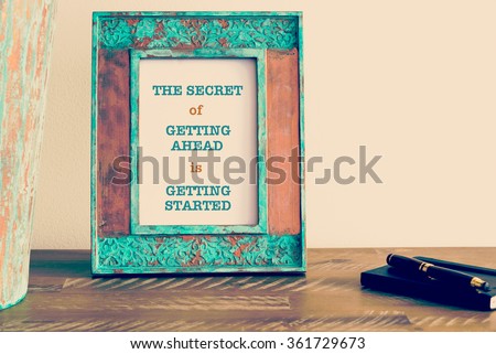 Retro effect and toned image of a vintage photo frame next to fountain pen and notebook . Motivational quote written with typewriter font THE SECRET OF GETTING AHEAD IS GETTING STARTED