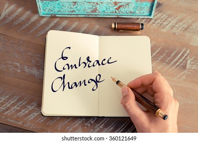 Retro effect and toned image of a woman hand writing a note with a fountain pen on a notebook. Motivational concept with handwritten text EMBRACE CHANGE