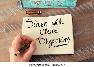 Retro effect and toned image of a woman hand writing a note with a fountain pen on a notebook. Handwritten text Start With Clear Objectives as business concept image