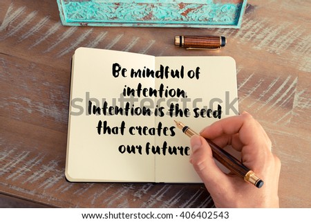 Retro effect and toned image of a woman hand writing on a notebook. Handwritten quote Be mindful of intention. Intention is the seed that creates our future.  as inspirational concept image