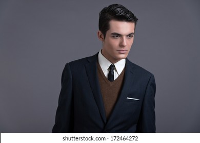 Retro Fifties Business Fashion Man With Dark Grease Hair. Wearing Dark Blue Suit And Tie. Studio Shot Against Grey.