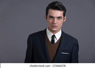 Retro Fifties Business Fashion Man With Dark Grease Hair. Wearing Dark Blue Suit And Tie. Studio Shot Against Grey.