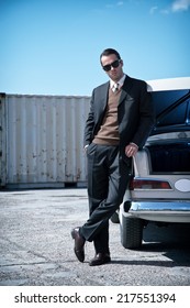 Retro Fifties Mafia Fashion Man Standing Next To Open Trunk Of Vintage Car.