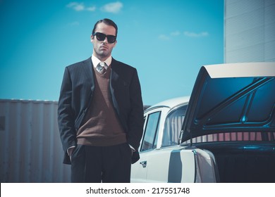 Retro Fifties Mafia Fashion Man Standing Next To Open Trunk Of Vintage Car.