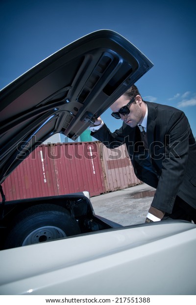 Retro fifties mafia fashion man looking in trunk of\
vintage car.