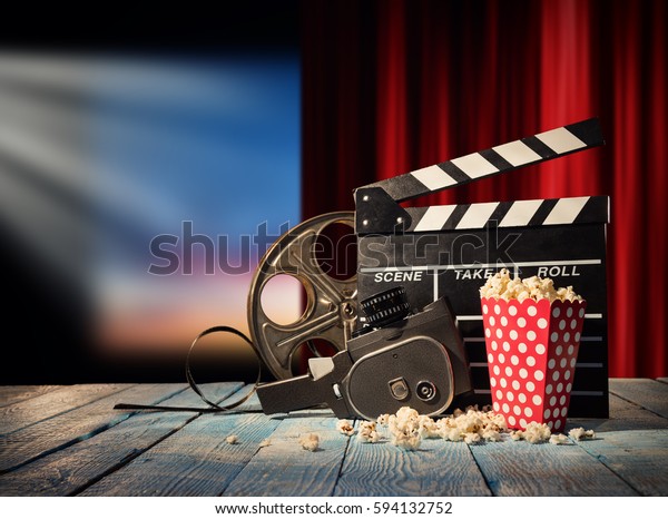 Retro film production accessories placed on\
wooden planks. Concept of film-making. Red curtain and movie screen\
on background