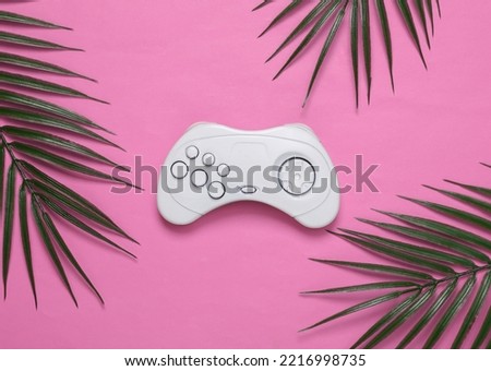 Retro gamepad and palm green leaves on pink background. Gaming concept. Tropical composition. Top view. Flat lay