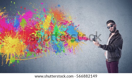 A retro hipster male taking photograph with a vintage camera of an urban wall with paint splatter concept