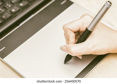 Retro image of female hand of a designer drawing with the stylus on a grey graphics tablet - Shutterstock ID 256450570