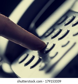 Retro image of a finger pressing a number button on the telephone to make a call.