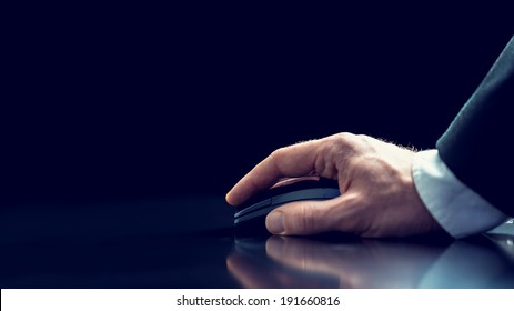 Retro Image Of The Hand Of A Businessman In A Suit Using A Wireless Computer Mouse On A Reflective Desktop Against A Dark Background With Copyspace.