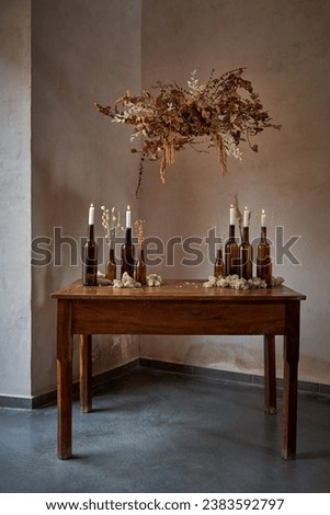 Retro interior of classic timber table with beer and wine bottles with lit candles and bouquet of dried flowers over