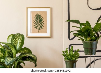 Retro interior design of living room with a lot of plants in green pots, vintage decor, accessoreis and gold mock up picture frame on the beige wall. Minimalistic concept of home decor. Template 
