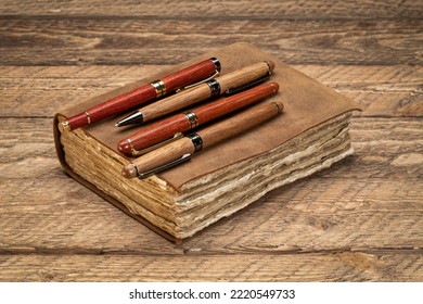 Retro Leather-bound Journal With Decked Edge Handmade Paper Pages And A Collection Of Stylish Pens On A Rustic Wooden Table, Writing And Journaling Concept