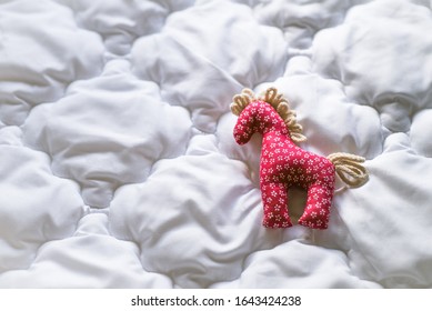 Retro little red cotton fabric horse toy decoration lying on a white fluffy feather blanket.  Country cottage home interior design background.