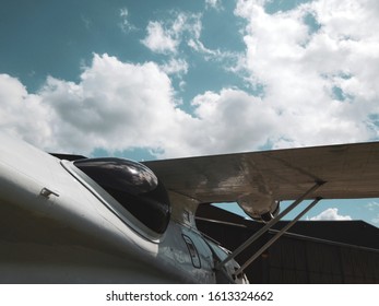 Retro Looking Airplane Cockpit & Wing, Outside A Hanger With Blue Sky With Clouds.