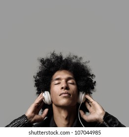 Retro Man With Afro Listening To Music On DJ Headphones With Eyes Closed. Isolated On Grey Background In Studio.