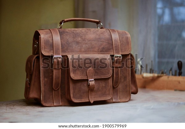 Retro men\'s work bag made\
of cowhide. Photo created in a bag workshop. In the background are\
bag work tools. Briefcase made of brown leather. Satchel to work.\
Bag for men.