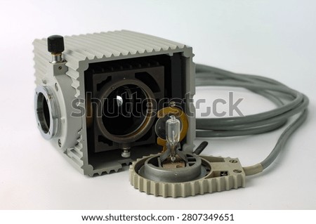 Retro microscope light source featuring a built-in condenser lens, metal housing and electrical power cord. Scientific optical equipment for laboratory microscopy isolated on white.