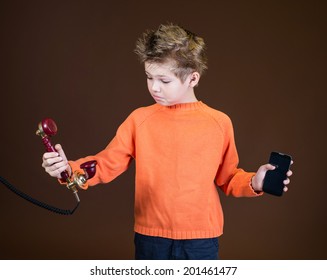 Retro And Modern Communication Symbols Concept - Cell And Rotary Phone. Confused Boy Holding Retro Rotary Telephone In One Hand And Cellphone In Other. Child With Conventional Telephone And Smartphone