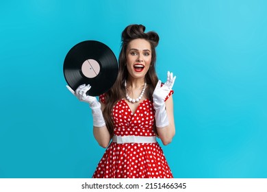 Retro Music, Old Songs, Nostalgia. Excited Young Pinup Woman In Retro Polka Dot Dress Holding Gramophone Vinyl Record, Smiling At Camera Over Blue Studio Background