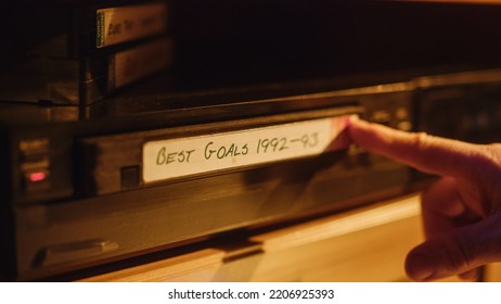 Retro Nineties Technology Concept. Close Up of a Person Inserting a VHS Cassette in a Player with Nostalgic Best Sport Goals Footage from World Cup. Old VCR Shot with Shallow Depth of Field and Bokeh.