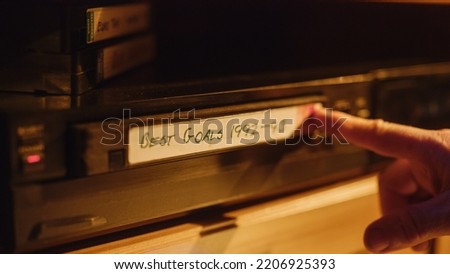 Retro Nineties Technology Concept. Close Up of a Person Inserting a VHS Cassette in a Player with Nostalgic Best Sport Goals Footage from World Cup. Old VCR Shot with Shallow Depth of Field and Bokeh.