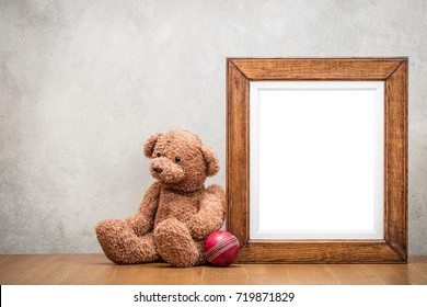Retro Oak Wooden Photo Frame Blank And Teddy Bear Toy With Leather Ball Front Old Textured Concrete Wall Background. Vintage Instagram Style Filtered Photography