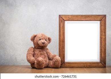 Retro Oak Wooden Photo Frame Blank And Teddy Bear Toy On Table Front Concrete Wall Background. Vintage Old Style Filtered Photography