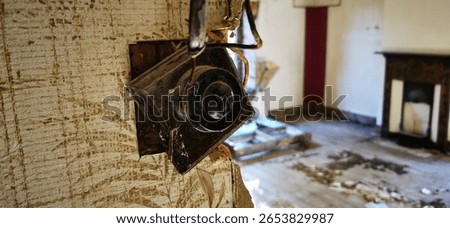 Retro obsolete light switch fitting in abandoned house. Derelict bulb controls broken hanging off wall. Bygone war-time era home in focus with background fireplace. Empty room, landlord disrepair.