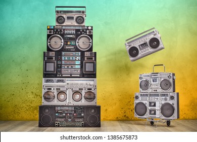Retro old design ghetto blaster boombox radio cassette tape recorders tower from circa 1980s, handcart front aged colored concrete wall background conceptual composition. Vintage style filtered photo