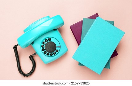 Retro Old Fashioned Blue Rotary Phone And Books On Pink Background. Top View