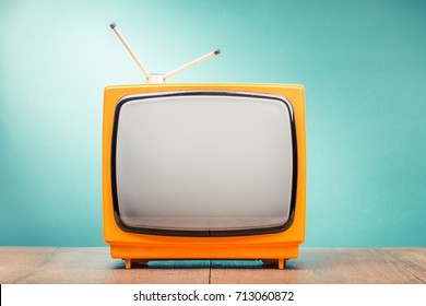 Retro old orange TV set receiver on wooden table front gradient mint green wall background. Vintage instagram style filtered photo