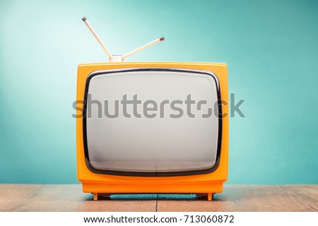 Retro old orange TV set receiver on wooden table front gradient mint green wall background. Vintage instagram style filtered photo