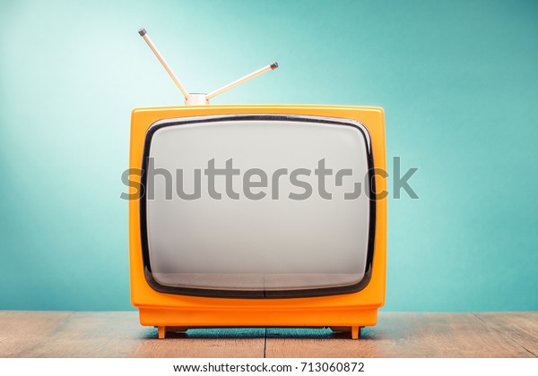 Retro old orange TV set receiver on wooden table\
front gradient mint green wall background. Vintage instagram style\
filtered photo