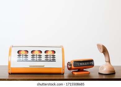 Retro old outdated classic telephone with orange table clock and retro patern bread box from circa 60s century on wooden stand white wall background for copy space. Vintage style filtered photo - Shutterstock ID 1715508685