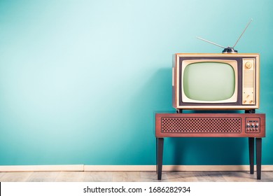 Ретро старый устаревший классический телевизионный приемник с телевизионной антенной около 60-х годов XX века на деревянной подставке с усилителем переднего градиента мятно-синего фона стены. Фото в винтажном стиле