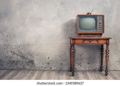 Retro old outdated TV receiver from circa 50s on wooden table front textured concrete wall background. Vintage style filtered photo