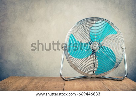 Retro old portable office or home cooling fan standing on desk front concrete wall background. Vintage instagram style filtered photo