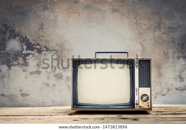 Retro old television on wood table\
with old concrete wall background. Vintage TV filter\
tone
