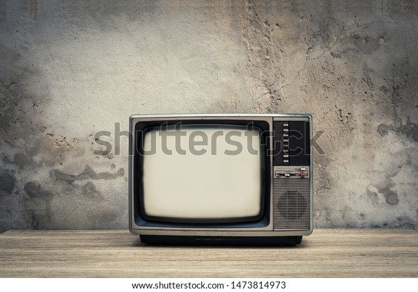Retro old television on wood table\
with old concrete wall background. Vintage TV filter\
tone