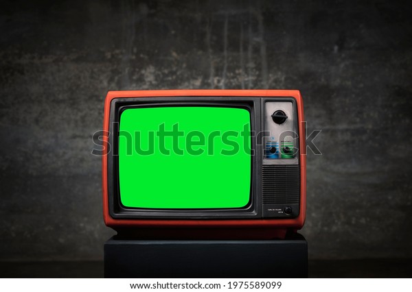 Retro old TV with green screen on wooden box\
in front of old wall\
background.