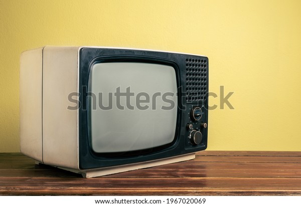 Retro old TV on wood table in\
front of yellow wall background. Vintage old style filtered\
photo