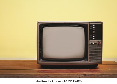 Retro Old Tv On Wooden Table With Yellow Concrete Wall Background.