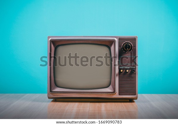 Retro old tv on wooden table with blue\
concrete wall background.