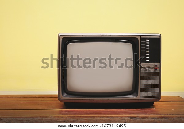 Retro old tv on wooden table with yellow\
concrete wall background.