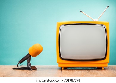 Retro old TV receiver and orange desk microphone on table front gradient mint green wall background. Broadcasting concept. Vintage style filtered photo - Shutterstock ID 701987398