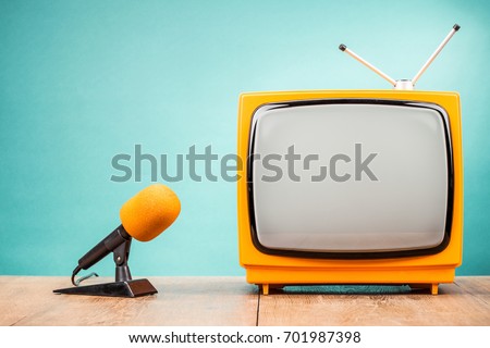 Retro old TV receiver and orange desk microphone on table front gradient mint green wall background. Broadcasting concept. Vintage style filtered photo