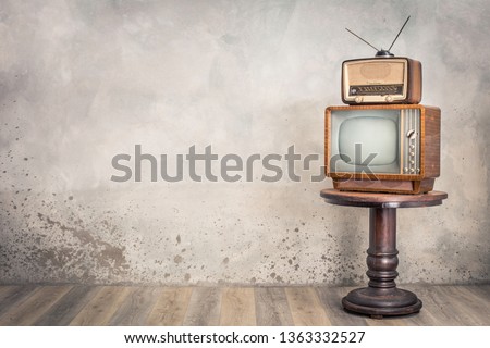 Retro old TV receiver and outdated broadcast radio from circa 50s on wooden table front textured concrete wall background. Vintage style filtered photo