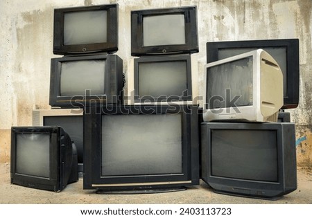 Retro old TVs pile on floor in front of old wall. Stack television sets with vintage filter effect.